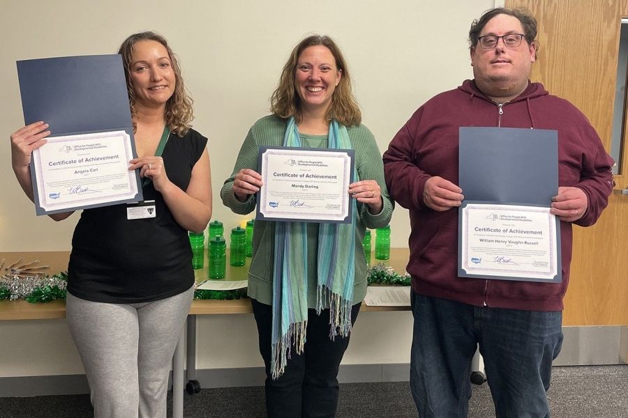 Three individuals standing, smiling, and holding certificates. 